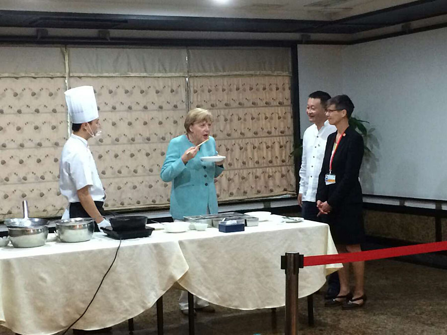 La chancelière allemande Angela Merkel discute avec à un vendeur lors de sa visite dans un marché ouvert à Chengdu, la capitale de la province du Sichuan (sud de la Chine), le 6 juillet 2014. Merkel a marqué de son empreinte le quotidien de la ville en visitant un marché ouvert et acheté un sac de fève pate pour 5 yuans (0,8 $). [Photo: Peng Chao/chinadaily.com.cn]