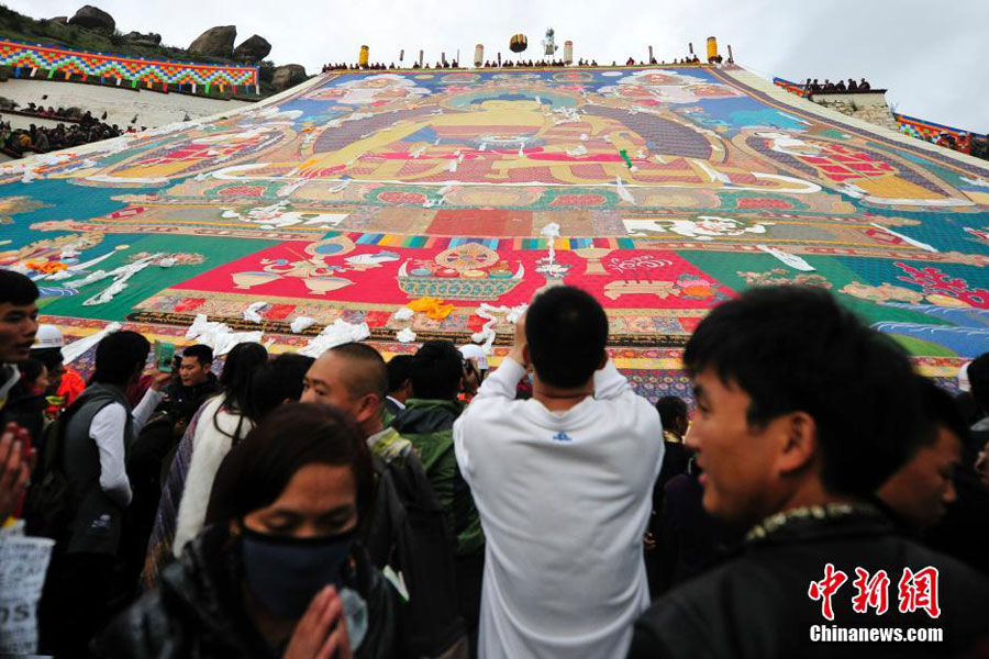 Les bouddhistes tibétains et les touristes admirent un tangka géant, une broderie ou peinture de soie religieuse propre au Tibet, lors du festival annuel de Shoton au monastère de Drepung à la périphérie de Lhassa, dans la région autonome du Tibet, le 25 ao?t 2014 [Photo/Chinanews.com]