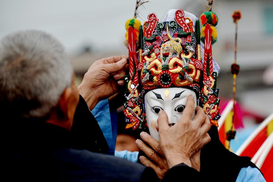 Photo prise le 15 mars, montrant un vieil homme aidant un acteur de l’Opéra d’Anshun à ajuster son masque avant de monter sur scène dans le village de Jiuxi, à Anshun dans la Province du Guizhou. [Photo / Xinhua]