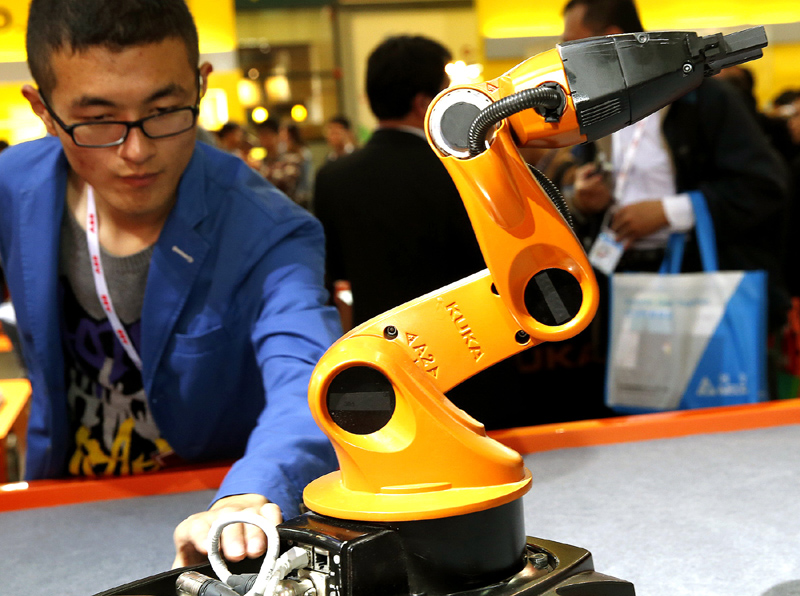 Un homme regarde un robot multifonctions con?u par la société de robotique allemande KUKA, exposé pendant le 16e Salon international de l'industrie de Chine à Shanghai, le 4 novembre 2014. [Photo/Xinhua]