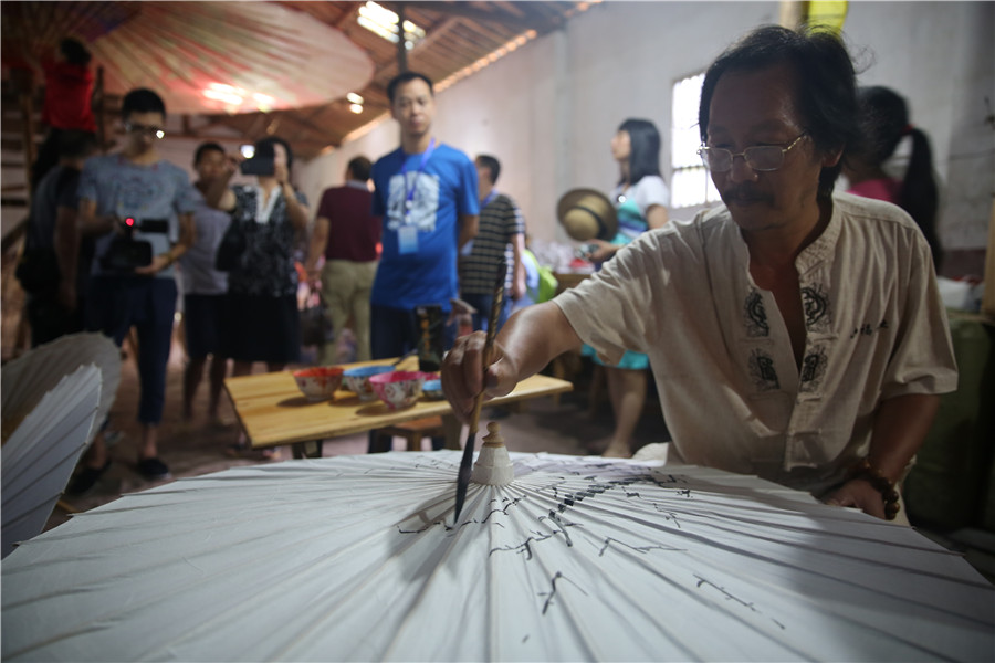 Un artiste peint un parapluie de papier huilé.