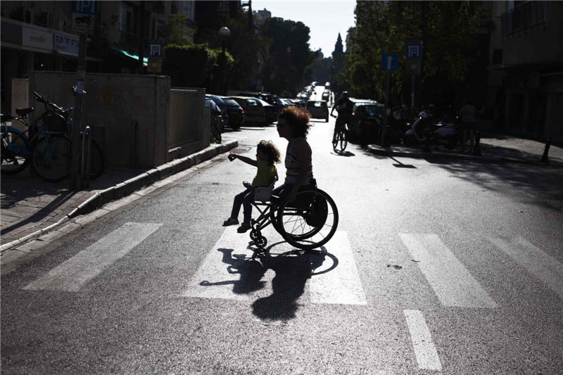 Pascale Bercovitch porte sa fille, Mica, agée de 3 ans, sur son fauteuil roulant alors qu'elles traversent une route près de leur maison à Tel-Aviv, le 16 mai 2012. Mme Bercovitch, 44 ans, qui a perdu ses jambes dans un accident de train en France en 1984, a représenté Isra?l lors des Jeux paralympiques de Londres dans l’épreuve de cyclisme à main.