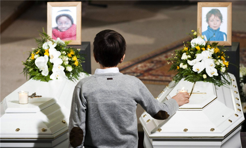 Un gar?on se tient debout près des cercueils de quelques-unes des victimes d'un accident de bus survenu en Suisse, lors d'une cérémonie à l'église Sint Pieters, à Louvain en Belgique, le22 mars 2012. Un bus transportant des élèves d’une école belge revenant d'un séjour au ski s'est écrasé sur le mur d'un tunnel à Sierre dans le Valais Suisse, tuant 28 personnes, dont 22 enfants, avait précisé la police le 14 mars.