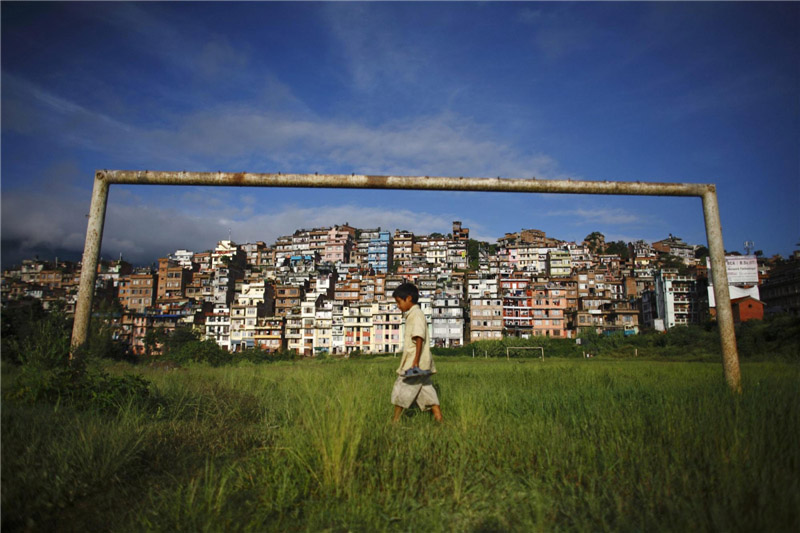 Un jeune gar?on passe devant un but de football près de l'ancienne ville de Kirtipur (derrière) à Katmandou, au Népal, le 12 ao?t 2012. Kirtipur est l'une des zones d'habitat populaire pour les étudiants et les professeurs habitant à l’extérieur de la ville.