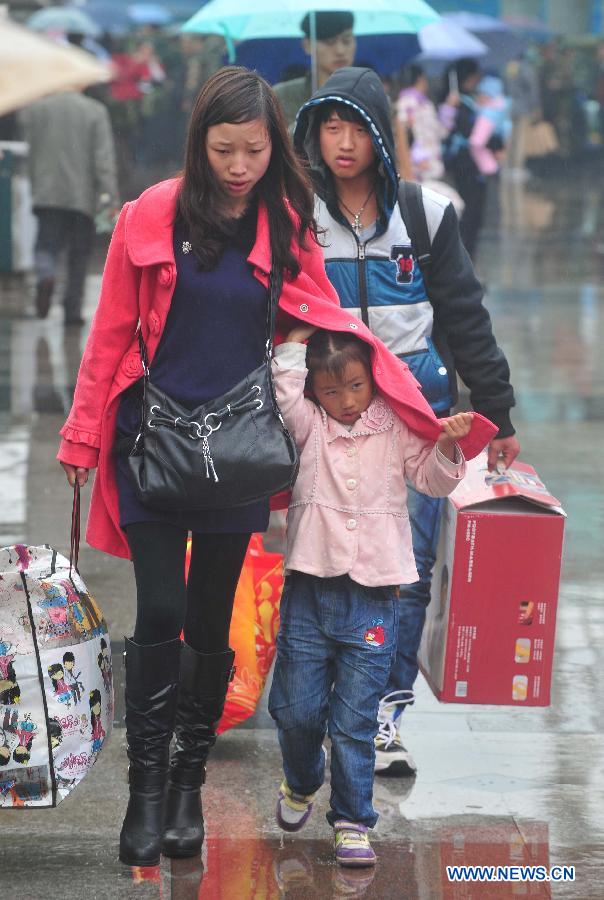 Le 26 janvier 2013, place de la gare de Nanning, capitale de la Région autonome Zhuang du Guangxi, une petite fille se cache sous la manteau de sa mère pour se protéger de la pluie. (Xinhua/Huang Xiaobang)