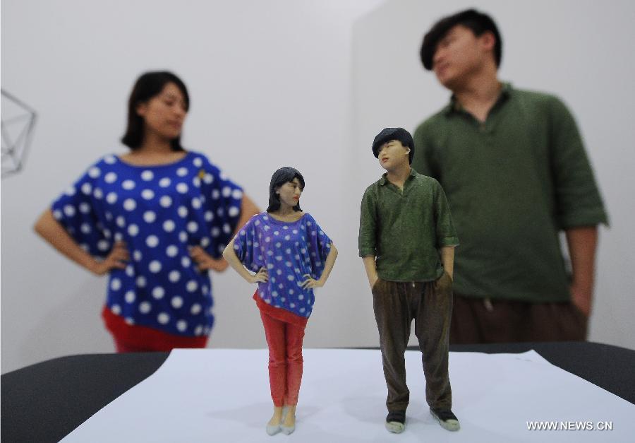 Un jeune couple pose pour la photo derrière des figurines imprimées en 3D d'eux-mêmes dans une boutique d'impression 3D qui vient d'ouvrir dans la municipalité de Chongqing, dans le Sud de la Chine, le 3 juin 2013. [Photo / Xinhua]