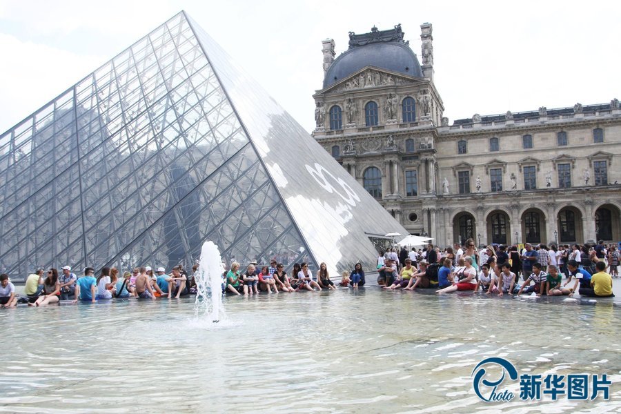 Le 19 juillet 2013, en proie à une vague de chaleur, de nombreux touristes se rafra?chissent autour de la fontaine devant le palais du Louvre.