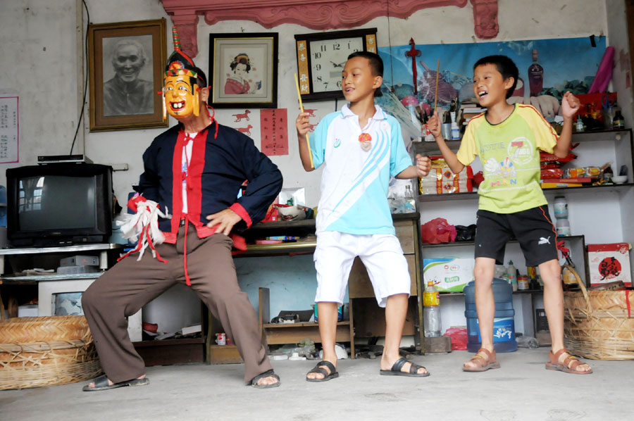 Le 18 ao?t 2013, dans le district autonome Maonan de Huanjiang dans la province du Guangxi, Tan Shengci enseigne la danse Nuo à deux gar?ons, qui suivent chez lui une formation de la fabrication des masques de cette danse. (Photo : Xinhua)