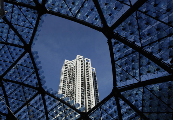 Une tour résidentielle est encadrée à l'intérieur d'une sculpture contenant 7000 bonbonnes d'eau recyclées avec des lumières LED, mesurant 20 mètres de diamètre et 10 mètres de hauteur, dans le parc Victoria de Hong Kong, le 10 septembre 2013. [Photo/agences]