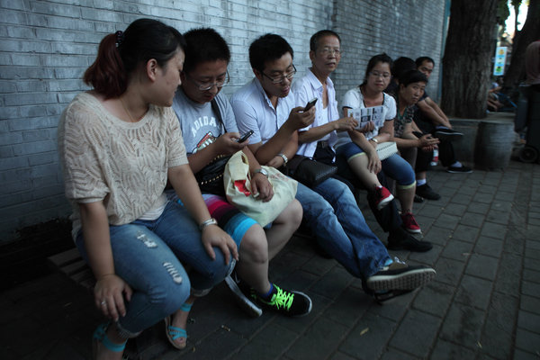 Des touristes jouent avec leur téléphone portable, lors d'une pause, dans une rue de Beijing, le 30 ao?t 2013.