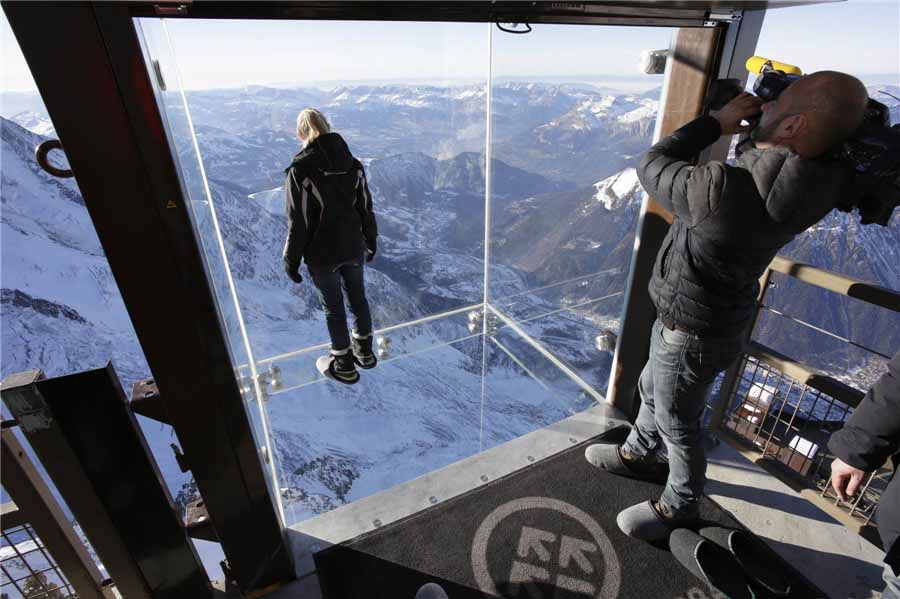 Les journalistes et les employés, portant des pantoufles pour protéger le plancher de verre, visitent l’installation ??Un pas dans le vide?? lors de la visite de presse au sommet de la montagne de l'Aiguille du Midi à Chamonix, dans les Alpes fran?aises, le 17 décembre 2013. [Photo / agences]