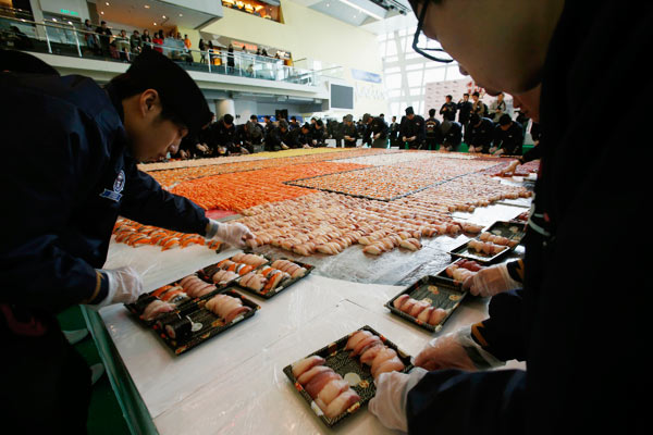 Des sushis vont être distribués gratuitement au public, après ce nouveau record du monde, en créant la plus grande mosa?que de sushis, ce à l'occasion du 10e anniversaire d'une cha?ne de magasins de sushi à Hong Kong, le 8 Janvier 2014. [Photo/agences]