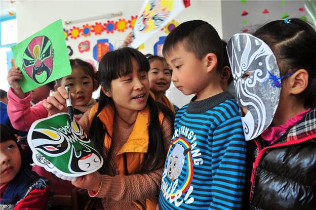 Une enseignante donne ses conseils aux enfants pour faire des masques d'opéra dans une école maternelle du Comté de Zigui, dans la Province du Hubei, le 26 mars 2014, pour célébrer la Journée mondiale du théatre.