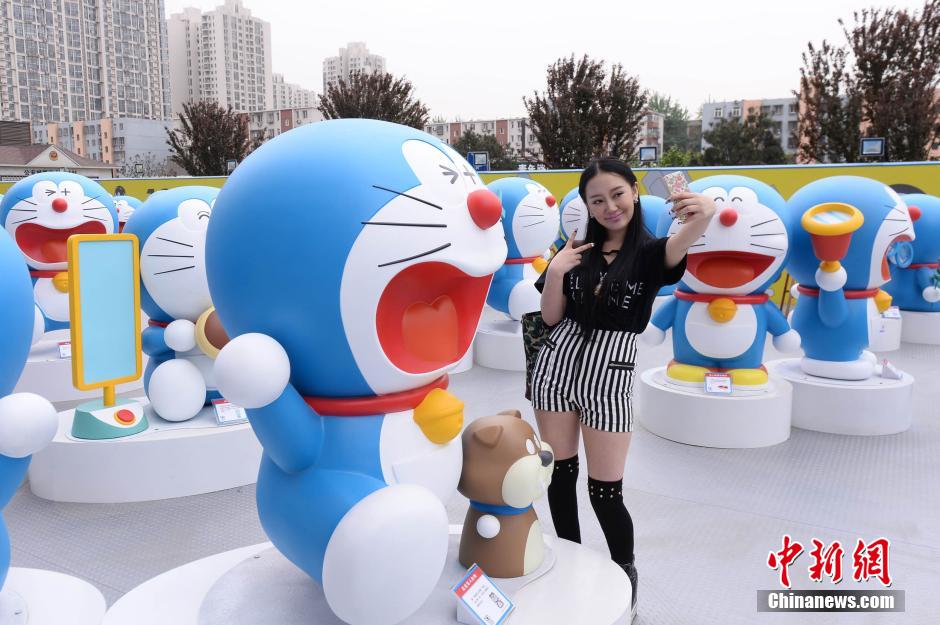 Mercredi 16 avril, devant le centre commercialJoy City du district de Chaoyang à Beijing, une visiteuse prend la pose avec des statues de Doraemon en pré-exposition. (Photo : Chinanews/Yi Ting)