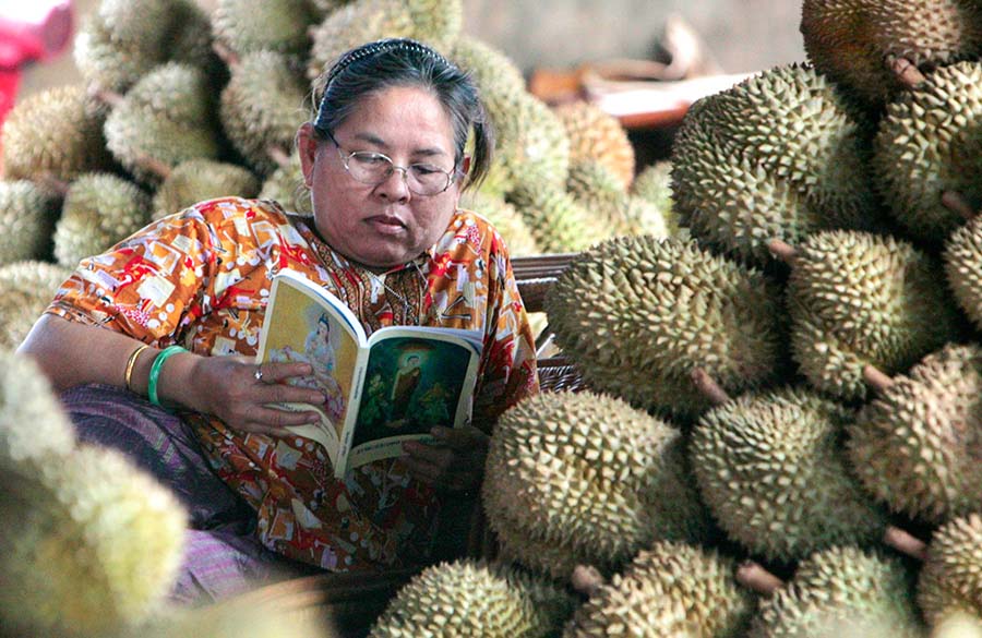 Le 17 juillet 2007, dans un marché de durian à Bangkok, une commer?ante en pleine lecture à c?té des tas de fruits. (Photo : Xinhua/Reuters)